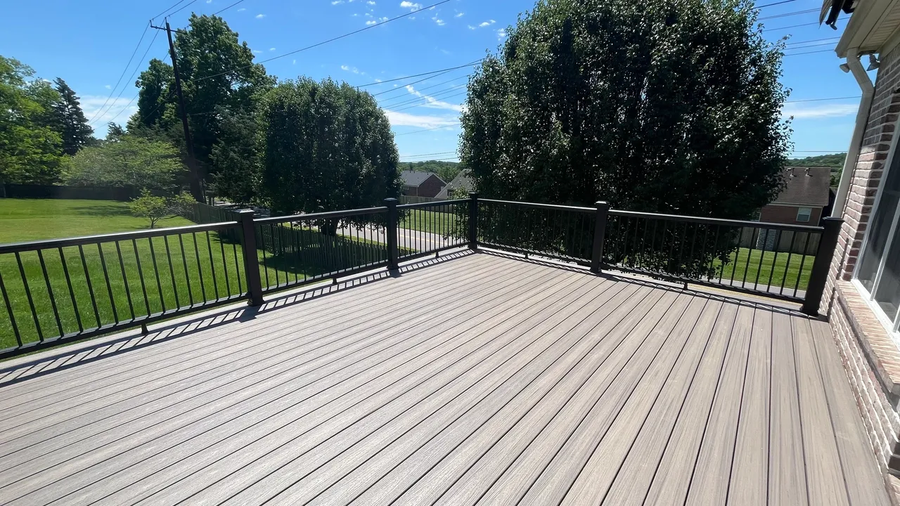 Spacious wooden deck with black railings and green trees in background.